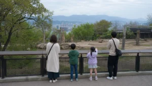 広島の丘陵にある動物園を思わせる園路からキリンを観察する家族