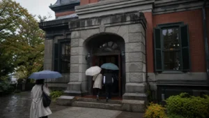 雨の末広町で歴史資料館を思わせる建物へ向かう旅行者