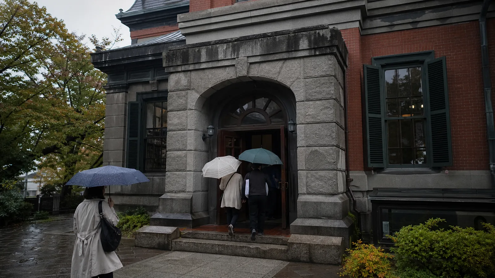 雨の末広町で歴史資料館を思わせる建物へ向かう旅行者
