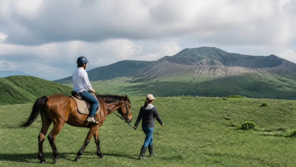 阿蘇を思わせる草原でスタッフに引かれた馬に乗る旅行者