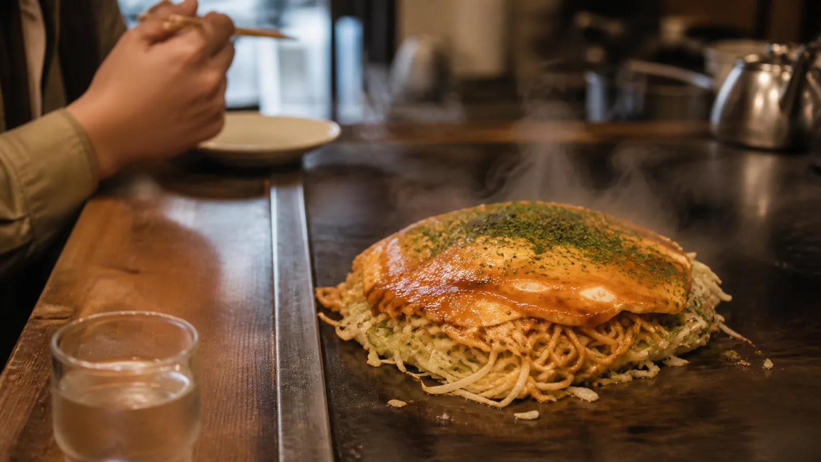 広島駅の鉄板カウンターで麺入りお好み焼きを待つ場面の編集イメージ