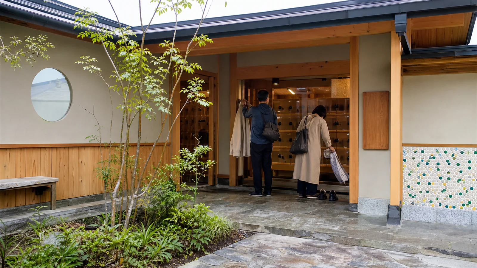 木と淡い壁の現代的な温泉館入口で入浴準備をする旅行者