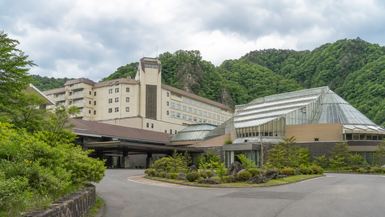 山あいに建つ大型温泉ホテルと屋内プール棟を表した無人の編集イメージ