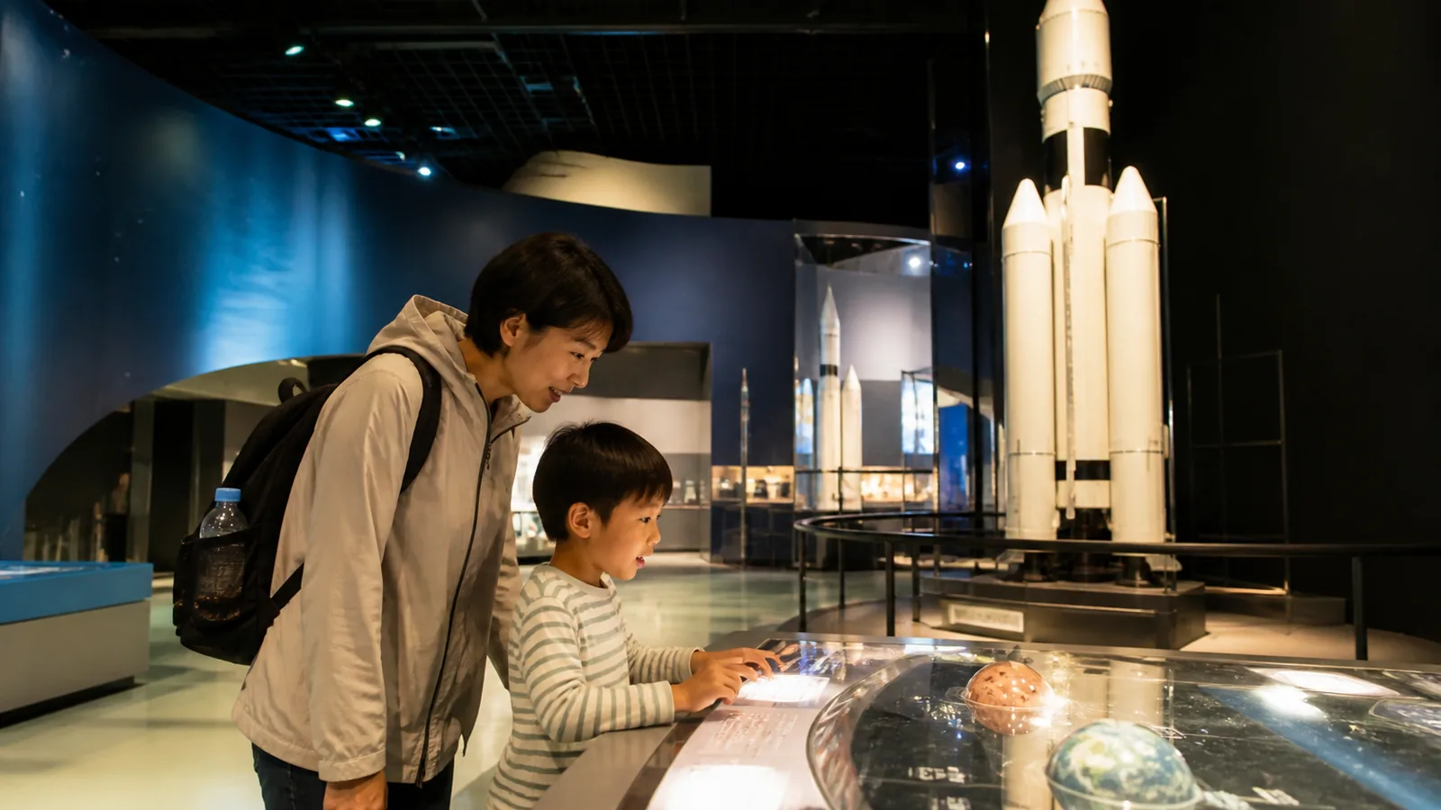 宇宙とロケットの体験展示を見る親子を表した科学館の編集イメージ