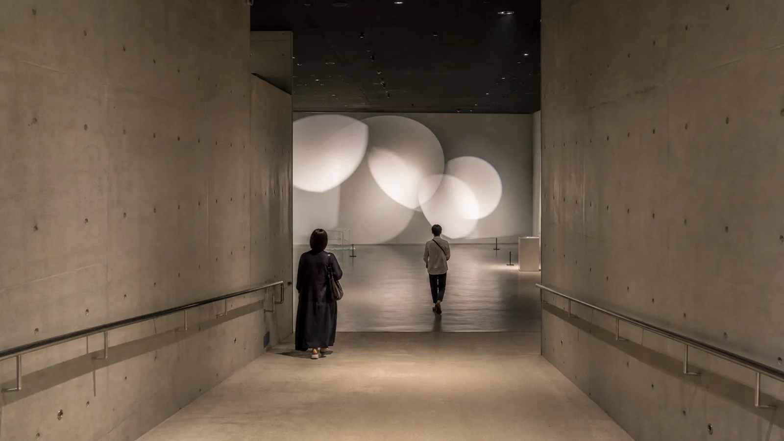 地下へ続く現代美術館の展示空間を歩く二人の編集イメージ