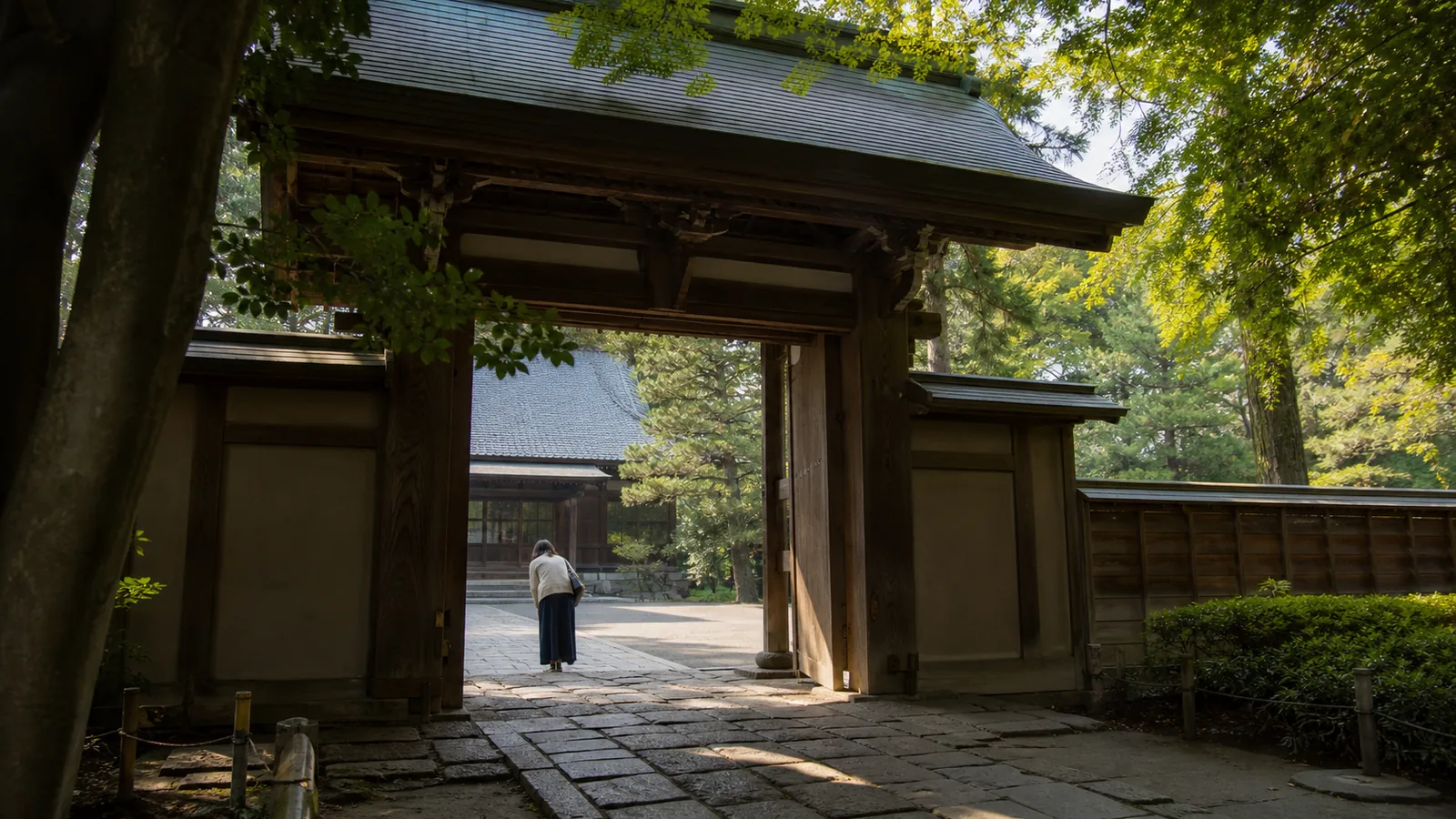 木立に囲まれた寺院の山門をくぐり一礼する旅行者の編集イメージ