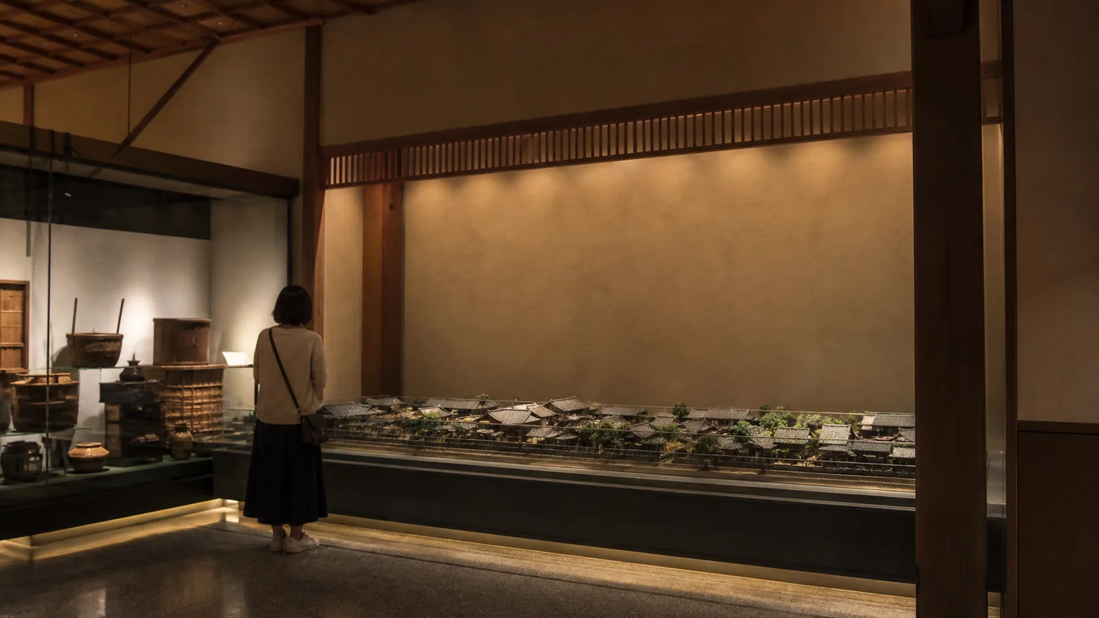落ち着いた和風博物館の展示導入空間で町並み模型を見る旅行者の編集イメージ