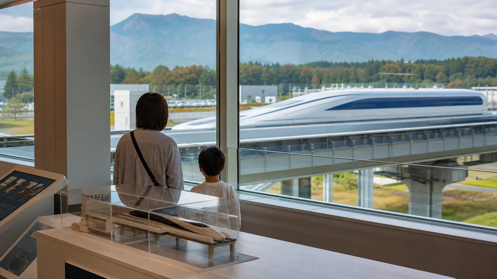 展示館の窓から親子がリニア車両を眺める編集イメージ