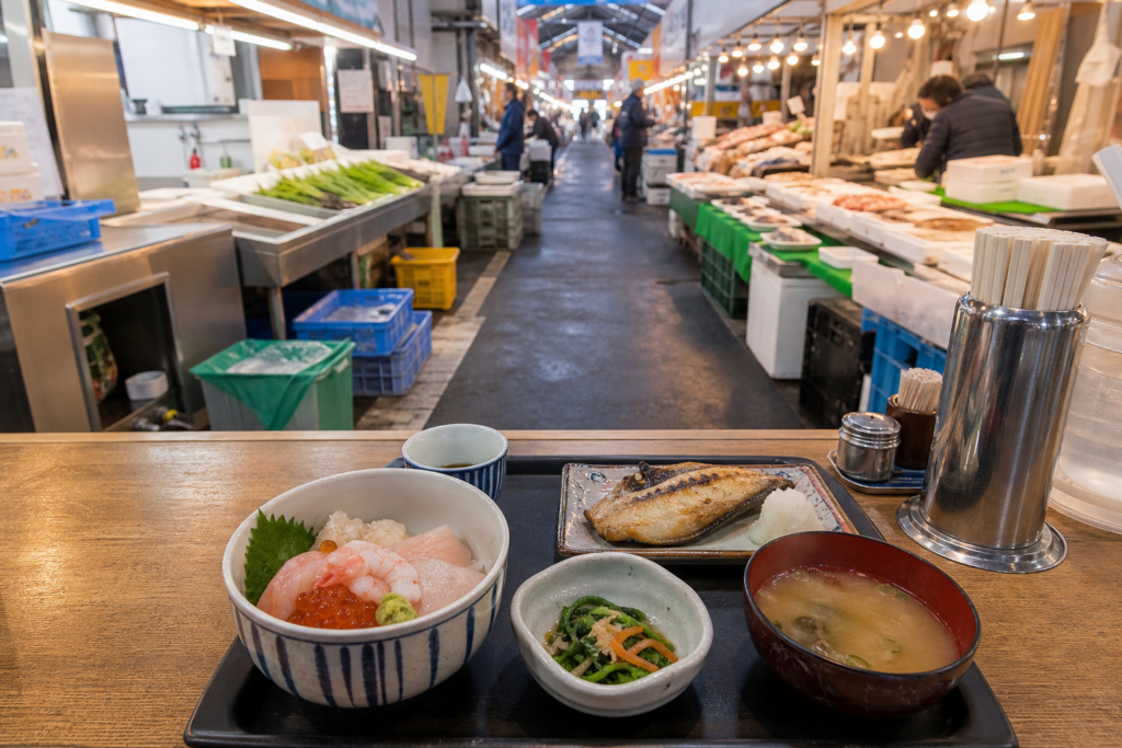 函館の市場通路を背景にした海鮮丼と焼き魚の朝食