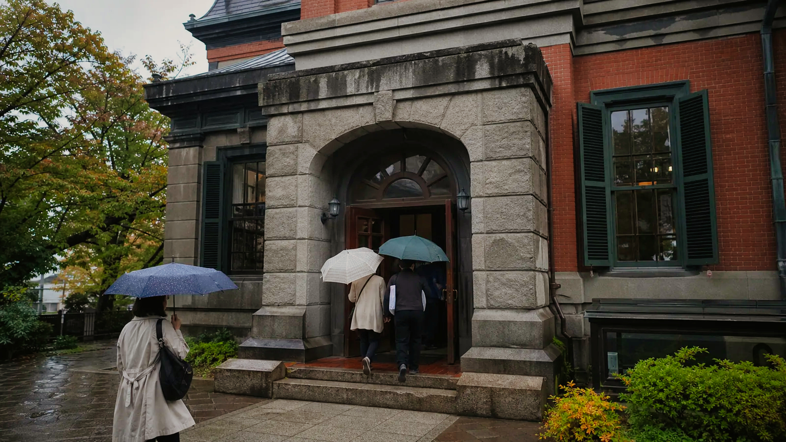 雨の末広町で歴史資料館を思わせる建物へ向かう旅行者