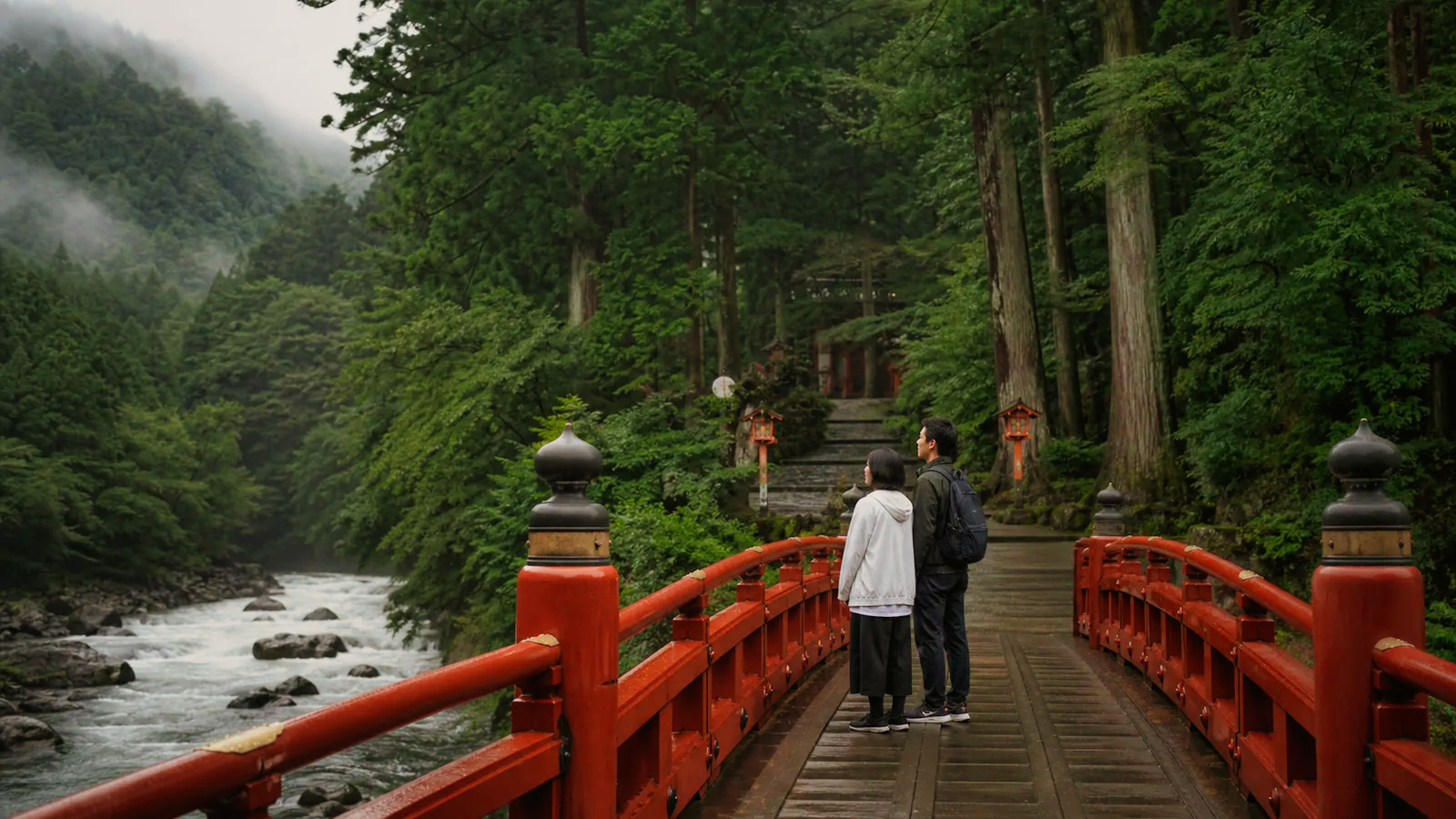日光山内の入口を思わせる朱塗りの橋と杉山を眺める旅行者