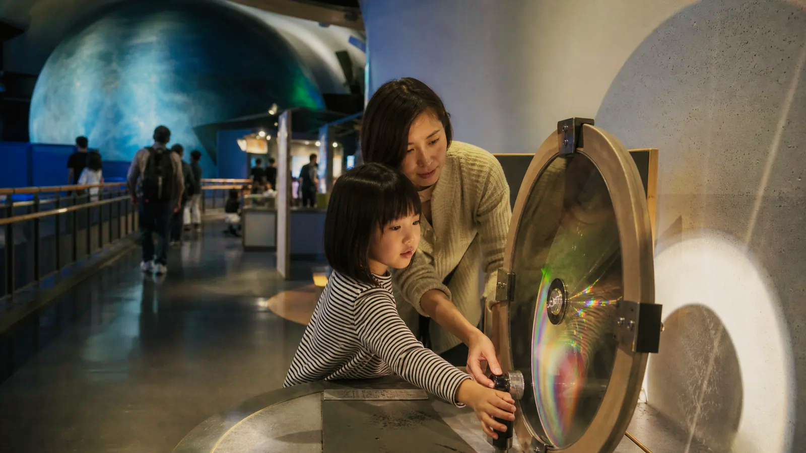 子ども向け科学館を思わせる屋内展示で光の実験を試す親子