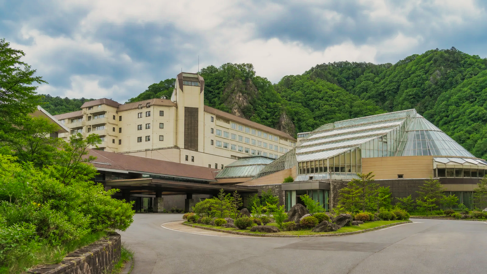山あいに建つ大型温泉ホテルと屋内プール棟を表した無人の編集イメージ