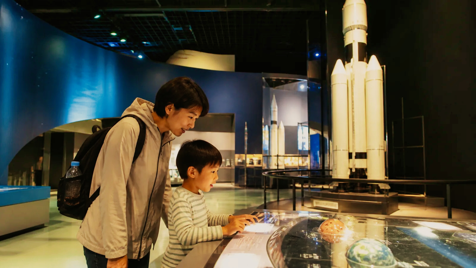宇宙とロケットの体験展示を見る親子を表した科学館の編集イメージ
