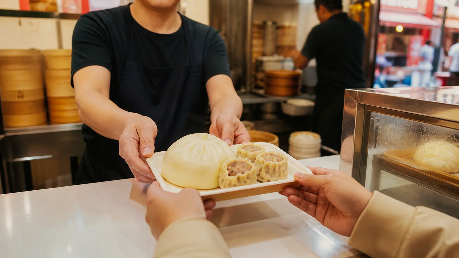南京町の店頭で豚まんと点心のトレーを受け取る旅行者
