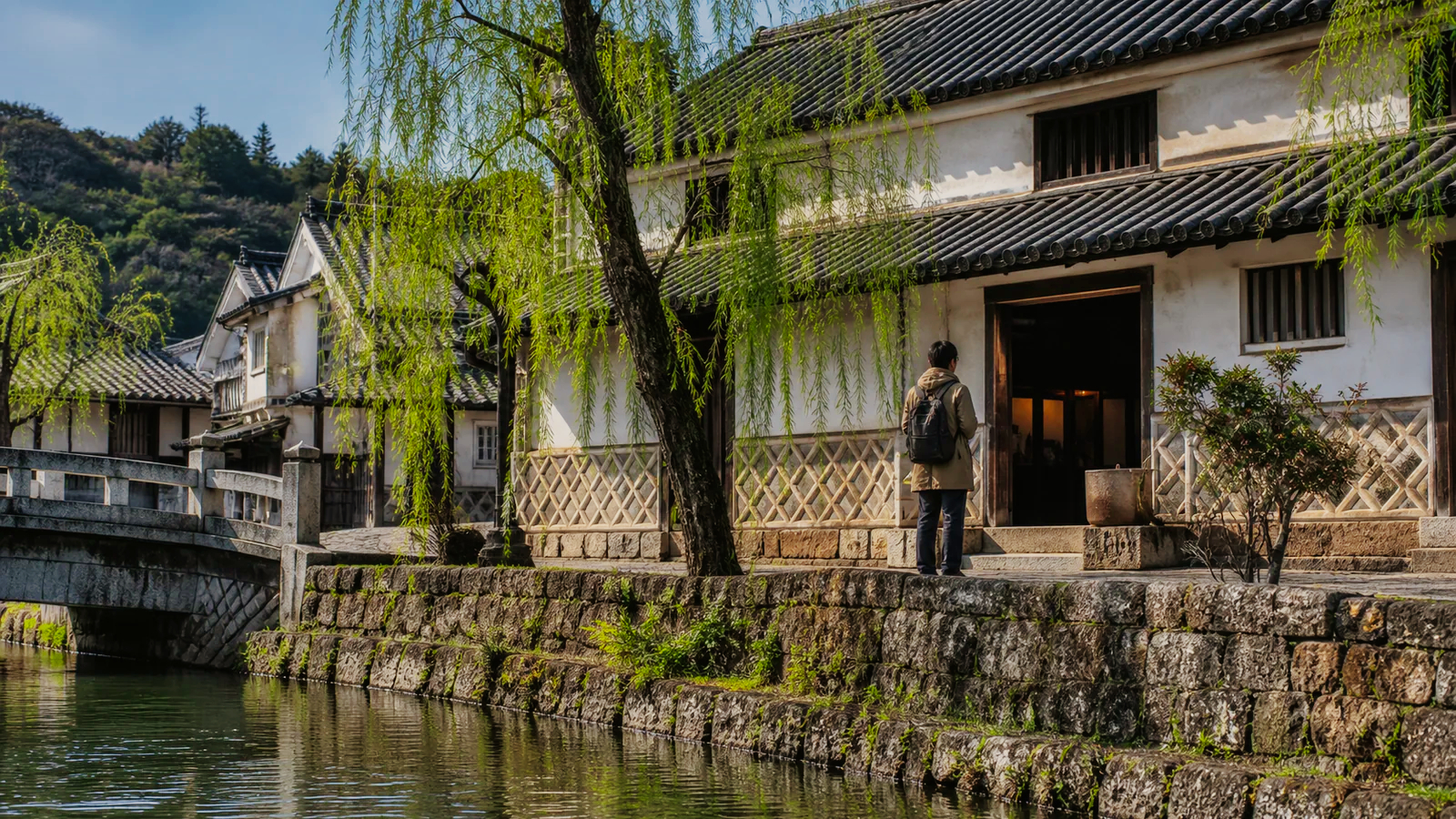 倉敷川沿いの白壁の土蔵建築へ歩く旅行者
