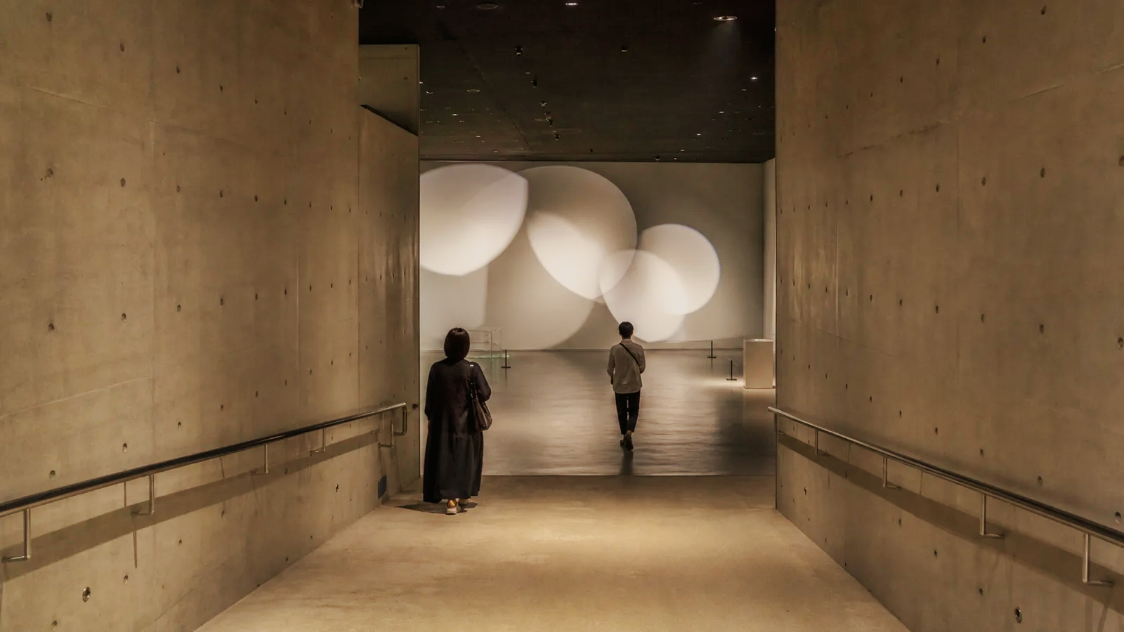 地下へ続く現代美術館の展示空間を歩く二人の編集イメージ