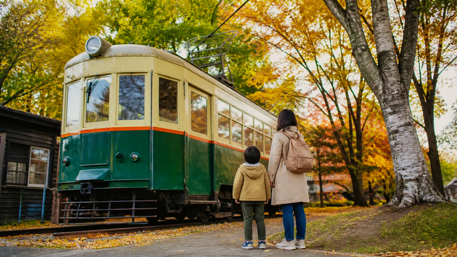 屋外に保存された昔の市電風車両を見上げる親子の編集イメージ