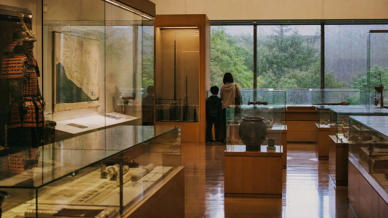 雨の窓を背景に歴史資料を展示する落ち着いた博物館内