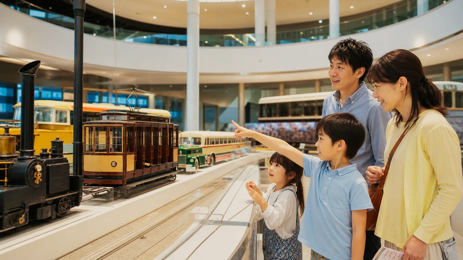 交通博物館を思わせる展示室で車両模型を指さす子どもと家族