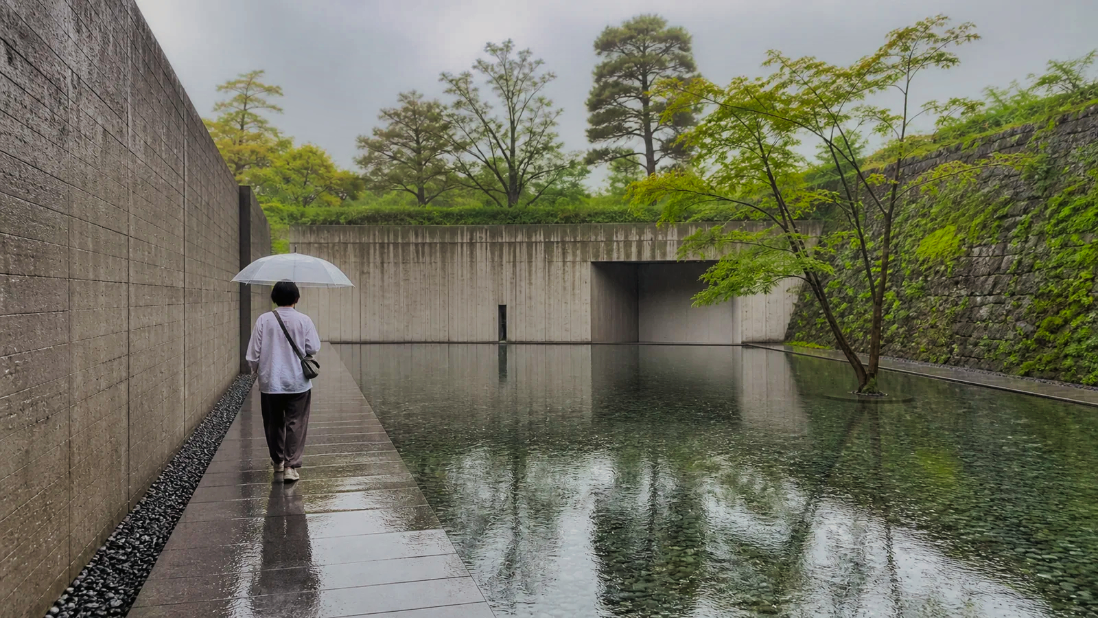 雨の水庭に沿って静かな文化施設を歩く旅行者
