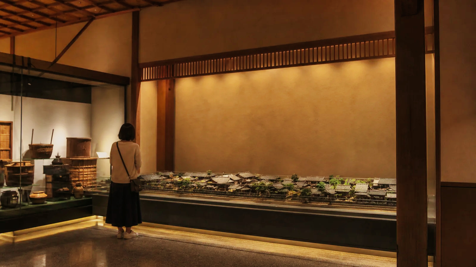 落ち着いた和風博物館の展示導入空間で町並み模型を見る旅行者の編集イメージ