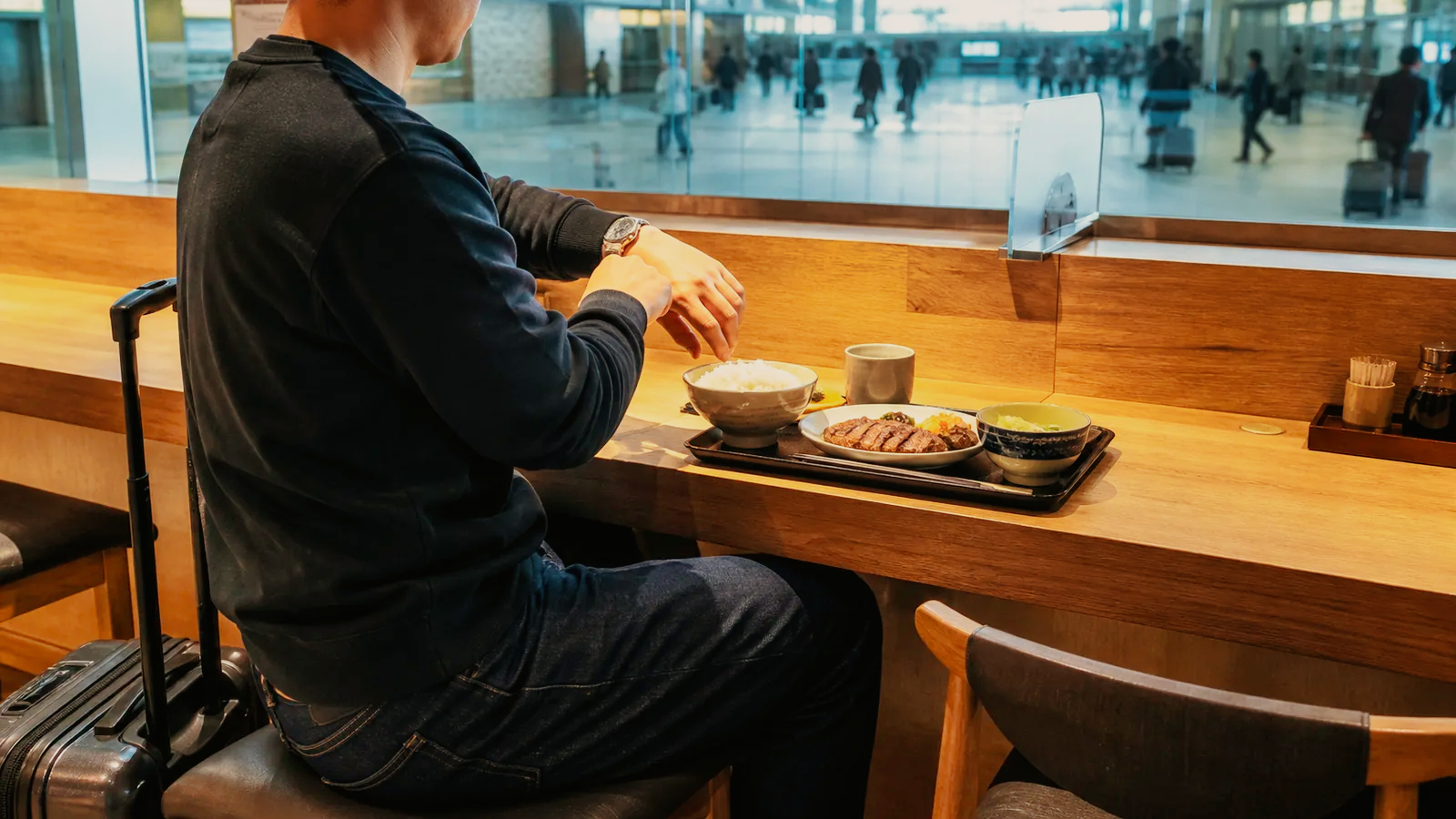 駅構内のカウンターで列車時刻を気にしながら牛たん定食を待つ旅行者の編集イメージ