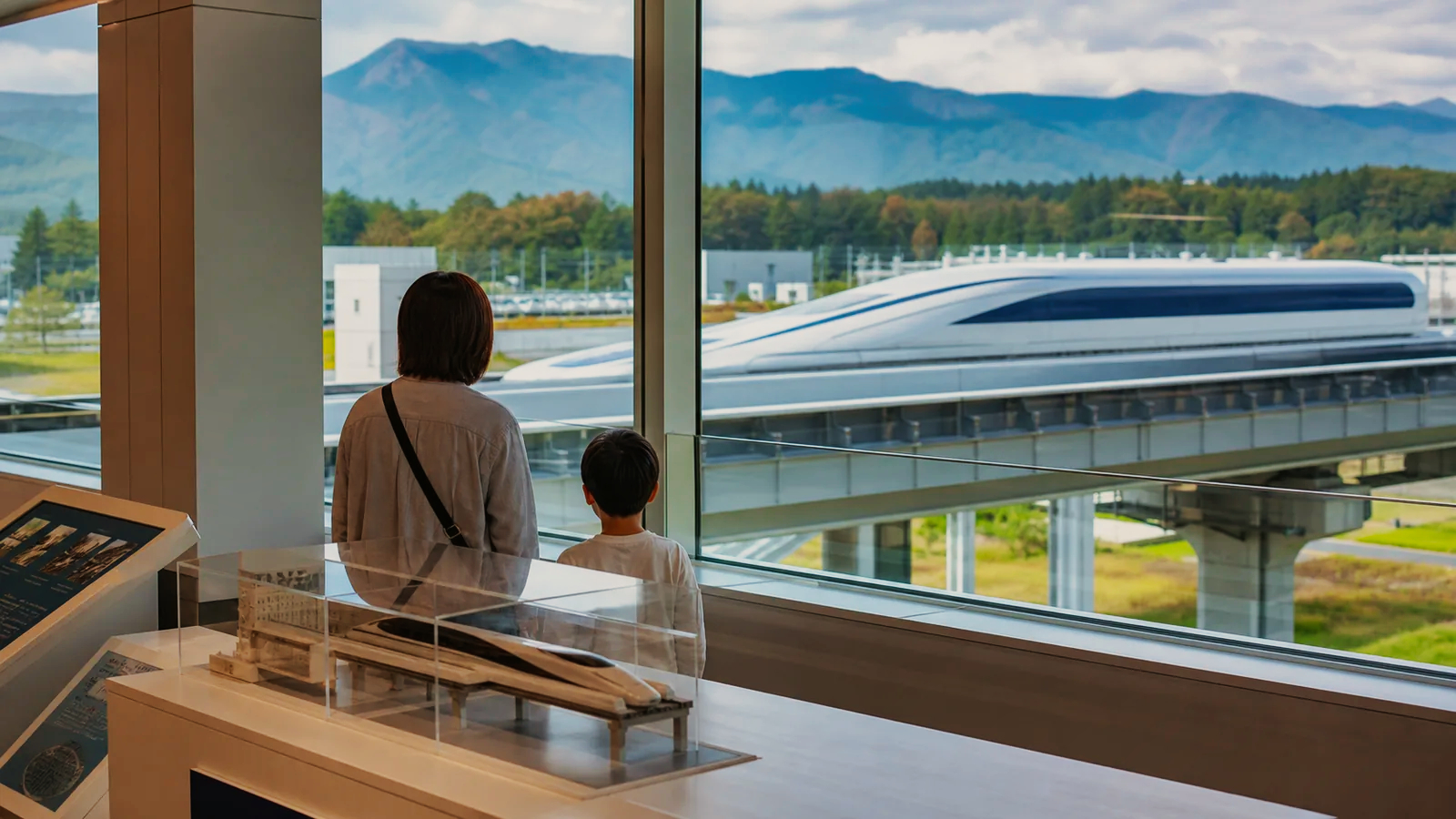展示館の窓から親子がリニア車両を眺める編集イメージ
