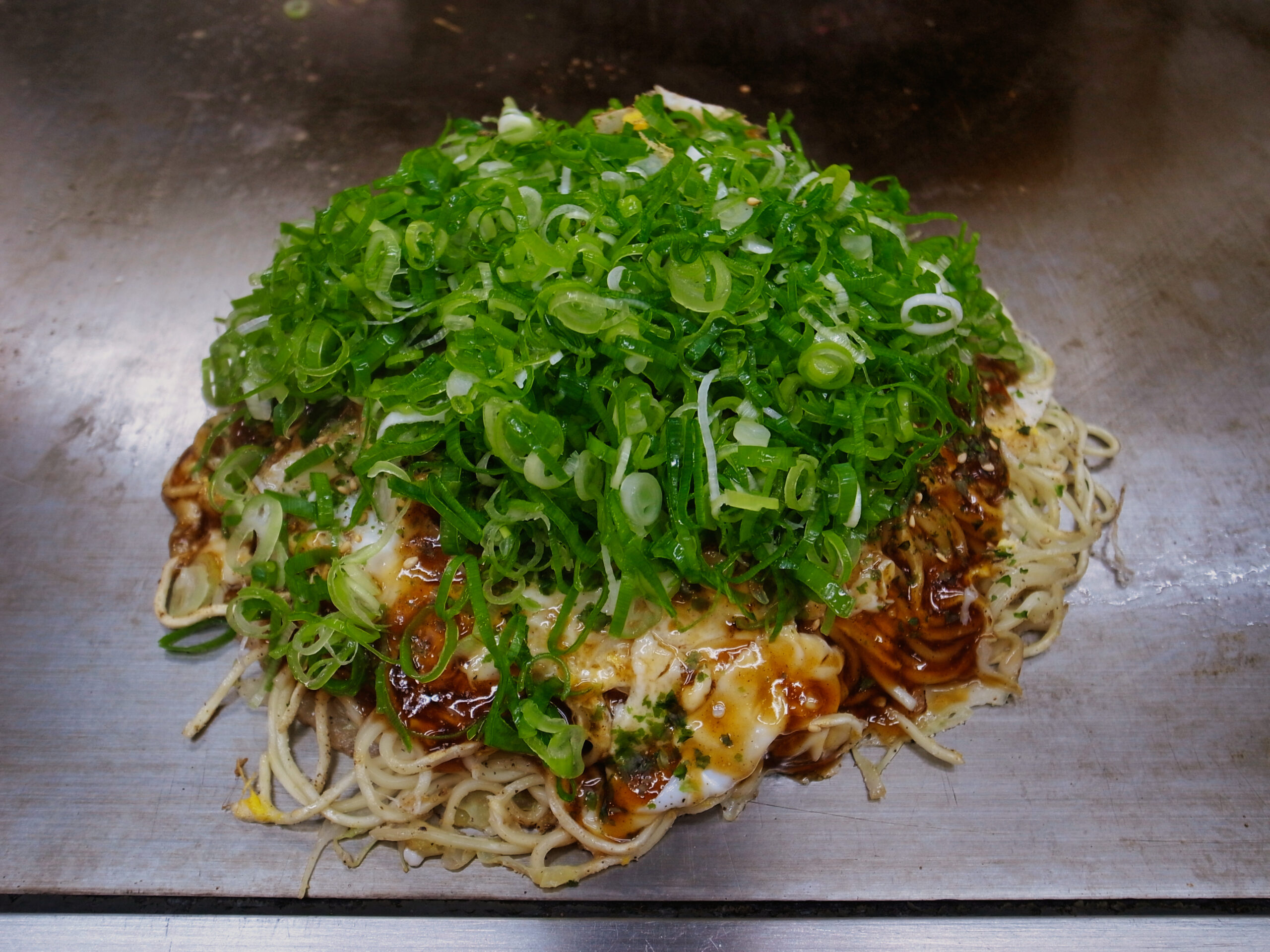 鉄板上の麺とネギを重ねた広島風お好み焼き（2011年撮影）