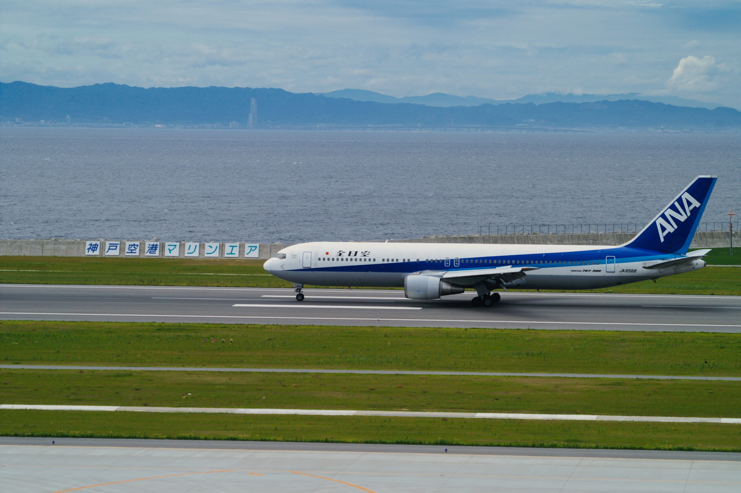 神戸空港の滑走路を走る旅客機と海・六甲山地